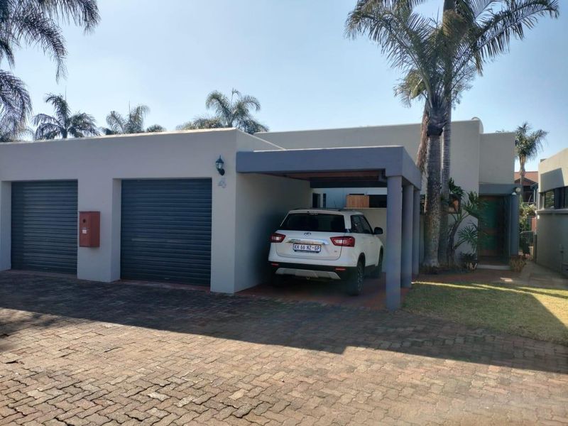 Front elevation of the townhouse featuring a double garage, a covered carport, and a paved driveway with established palm trees.