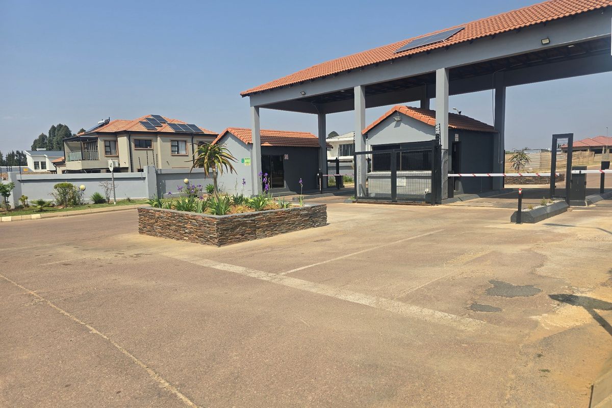 The entrance to the residential estate features a secure gatehouse, boom gate access, paved driveway, and well-maintained perimeter walling with electric fencing.