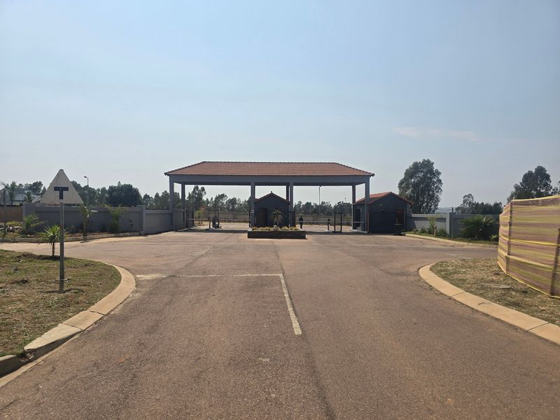A view of the secure gated entrance to the residential estate, featuring a paved driveway and established perimeter walling.