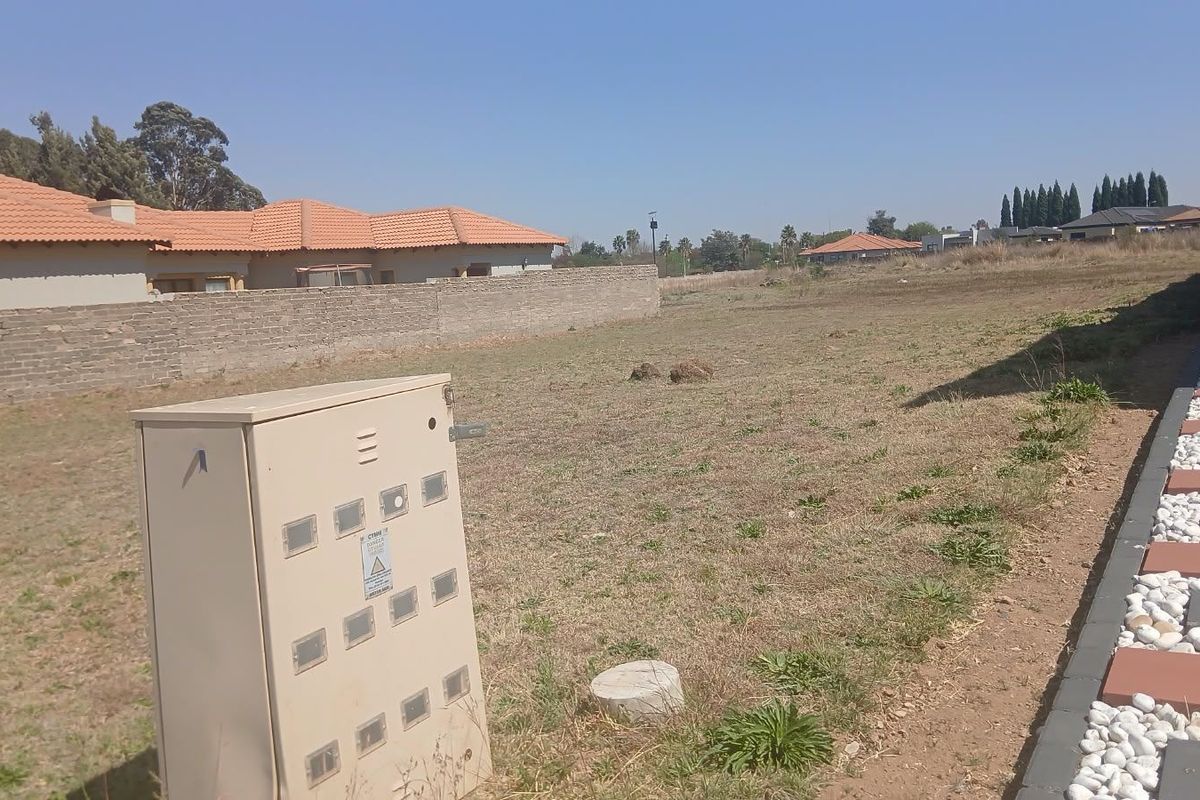 A vacant residential plot featuring a paved walkway, boundary wall, and an electrical distribution box, offering a clear space for future development.