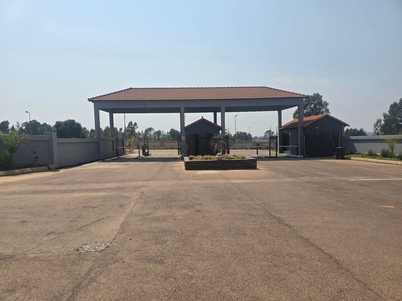 A secure gated entrance to the residential estate featuring a guardhouse, boom gates, and paved driveway access.
