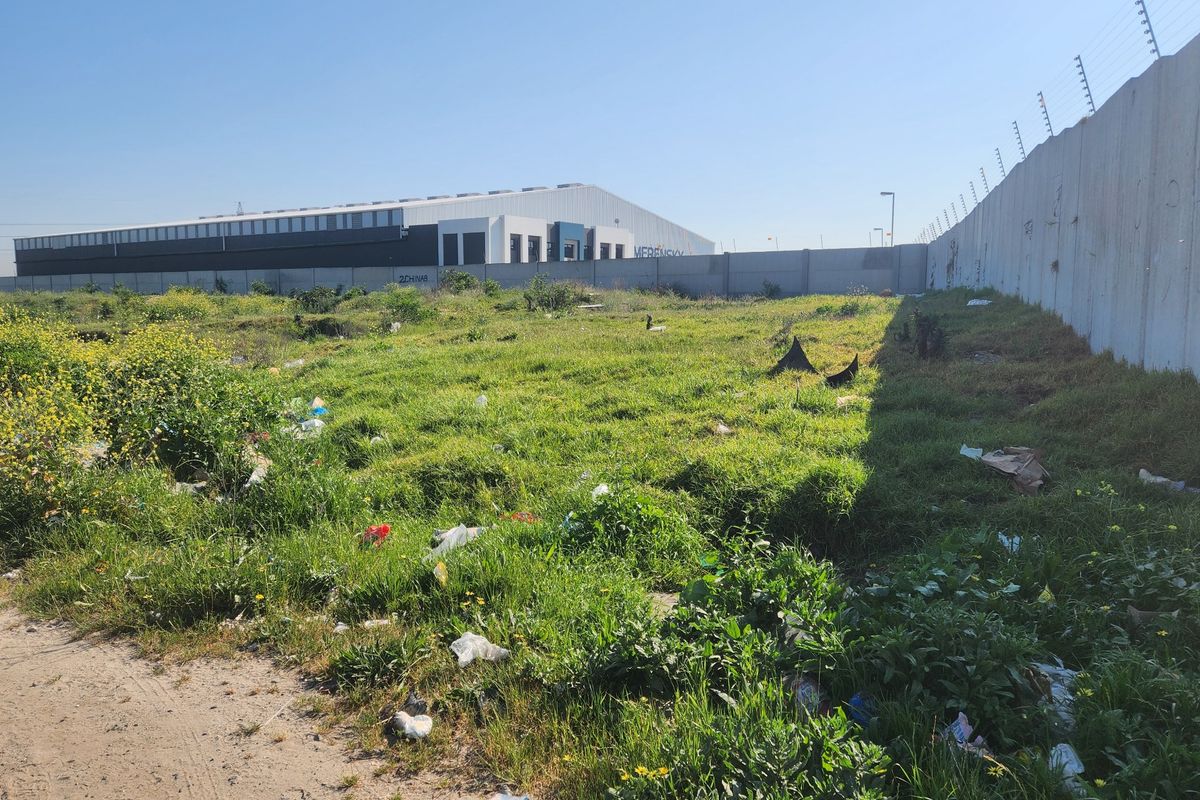Vacant residential land featuring a precast concrete boundary wall with electric fencing, currently requiring clearing of overgrown vegetation and debris.