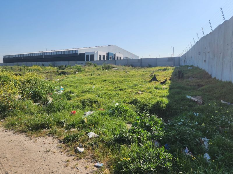 Vacant residential land featuring a precast concrete boundary wall with electric fencing, currently requiring clearing of overgrown vegetation and debris.