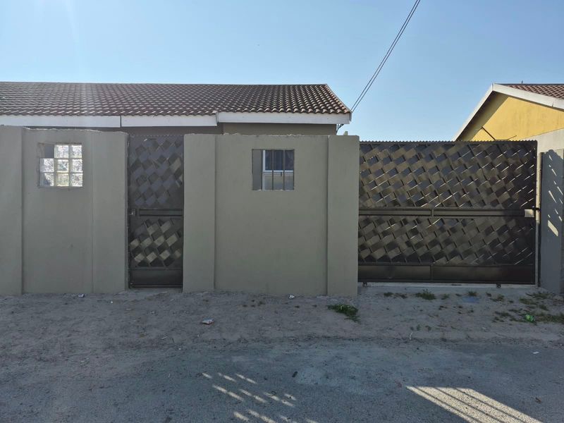 Front exterior view of the property featuring a secure perimeter wall with a metal pedestrian gate and a sliding driveway gate.