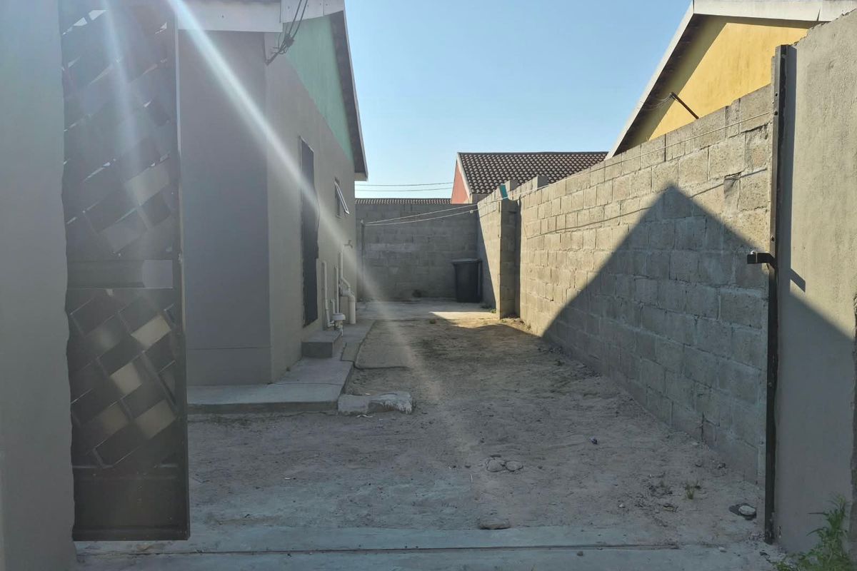 A side yard area featuring a concrete block boundary wall, metal gate, and unpaved ground, offering potential for landscaping or paving improvements.