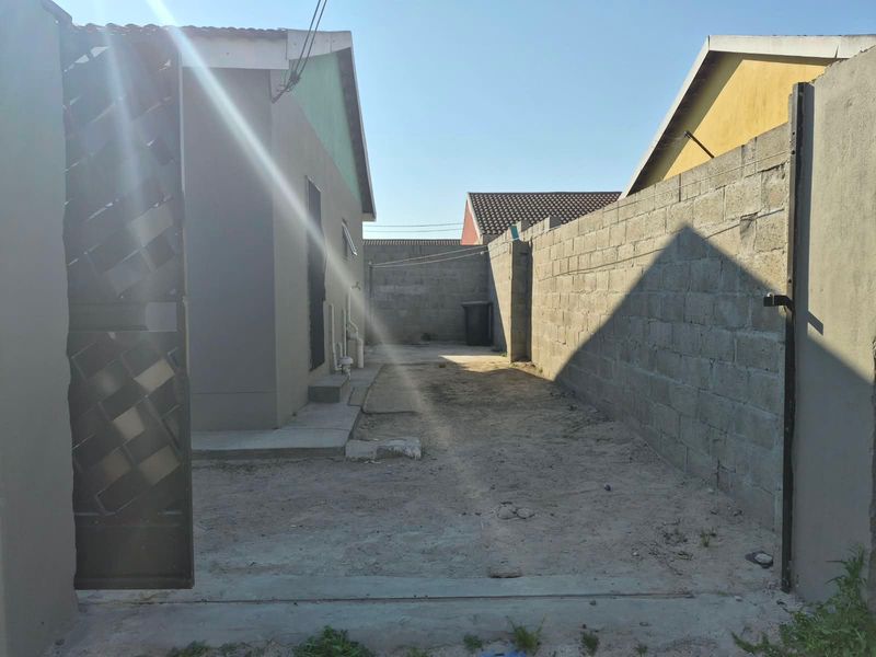 A side yard area featuring a concrete block boundary wall, metal gate, and unpaved ground, offering potential for landscaping or paving improvements.
