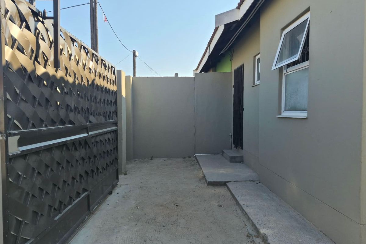 A side or rear exterior area featuring a metal security gate, perimeter wall, and concrete pathway leading to a side entrance.