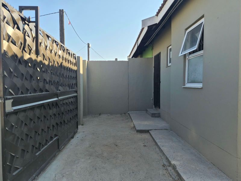 A side or rear exterior area featuring a metal security gate, perimeter wall, and concrete pathway leading to a side entrance.