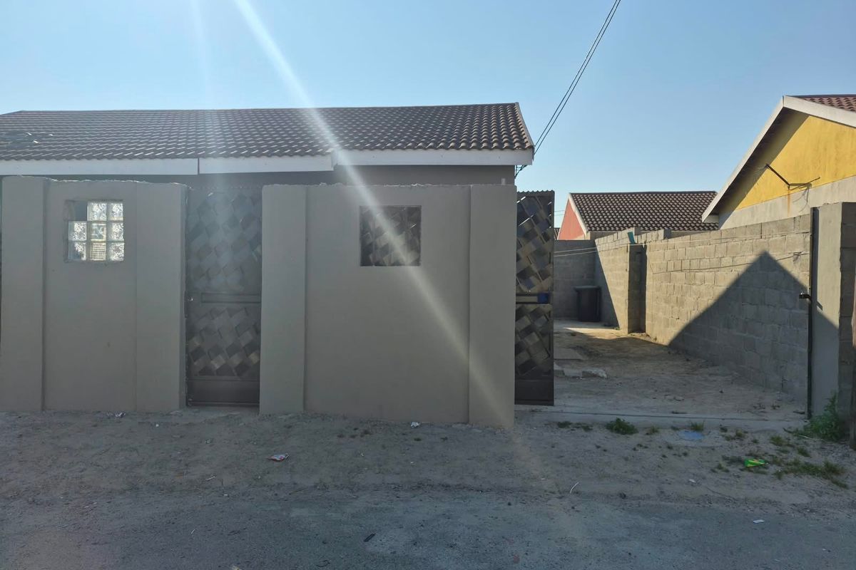 Front exterior view of a residential property featuring a tiled roof, boundary wall with security gate, and an unpaved driveway area.