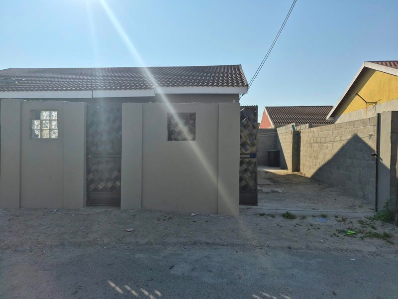 Front exterior view of a residential property featuring a tiled roof, boundary wall with security gate, and an unpaved driveway area.