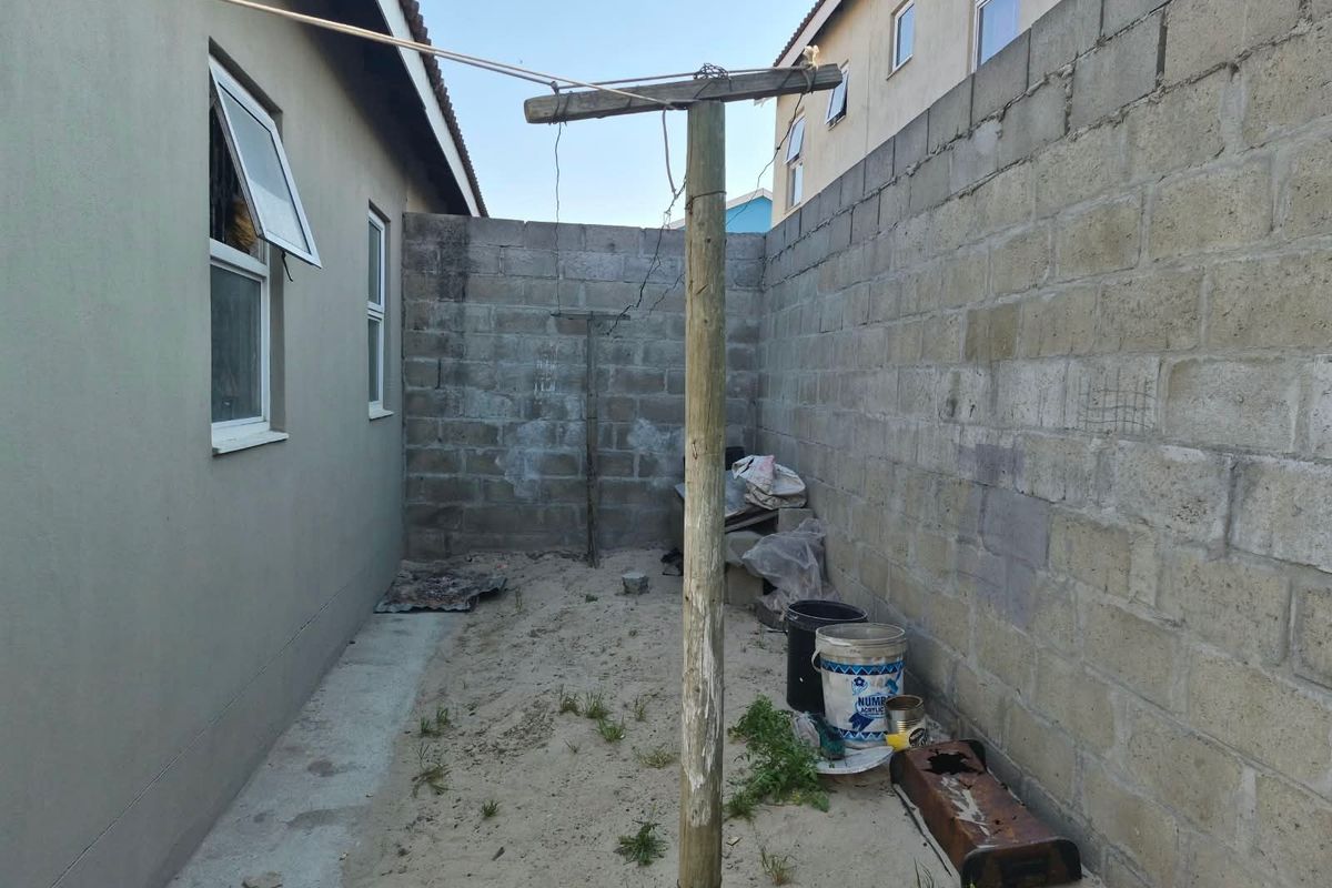 A side yard area featuring a concrete block boundary wall, casement windows, and a central clothesline pole, requiring landscaping and surface finishing.