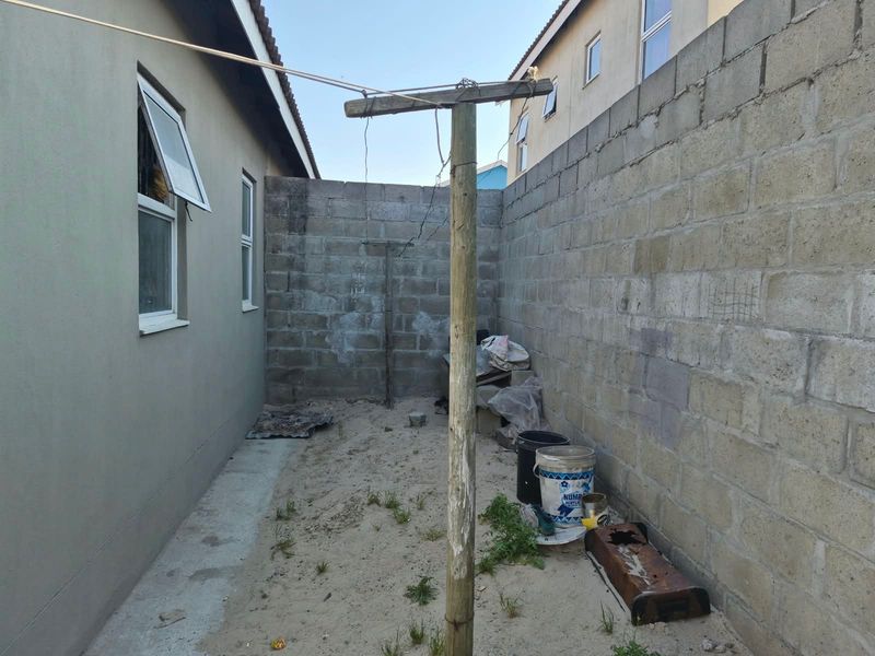 A side yard area featuring a concrete block boundary wall, casement windows, and a central clothesline pole, requiring landscaping and surface finishing.