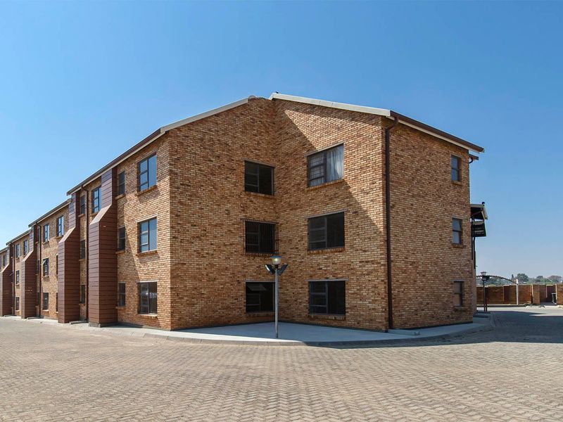 A multi-story apartment building featuring a face brick exterior, paved driveway, and secure window installations.