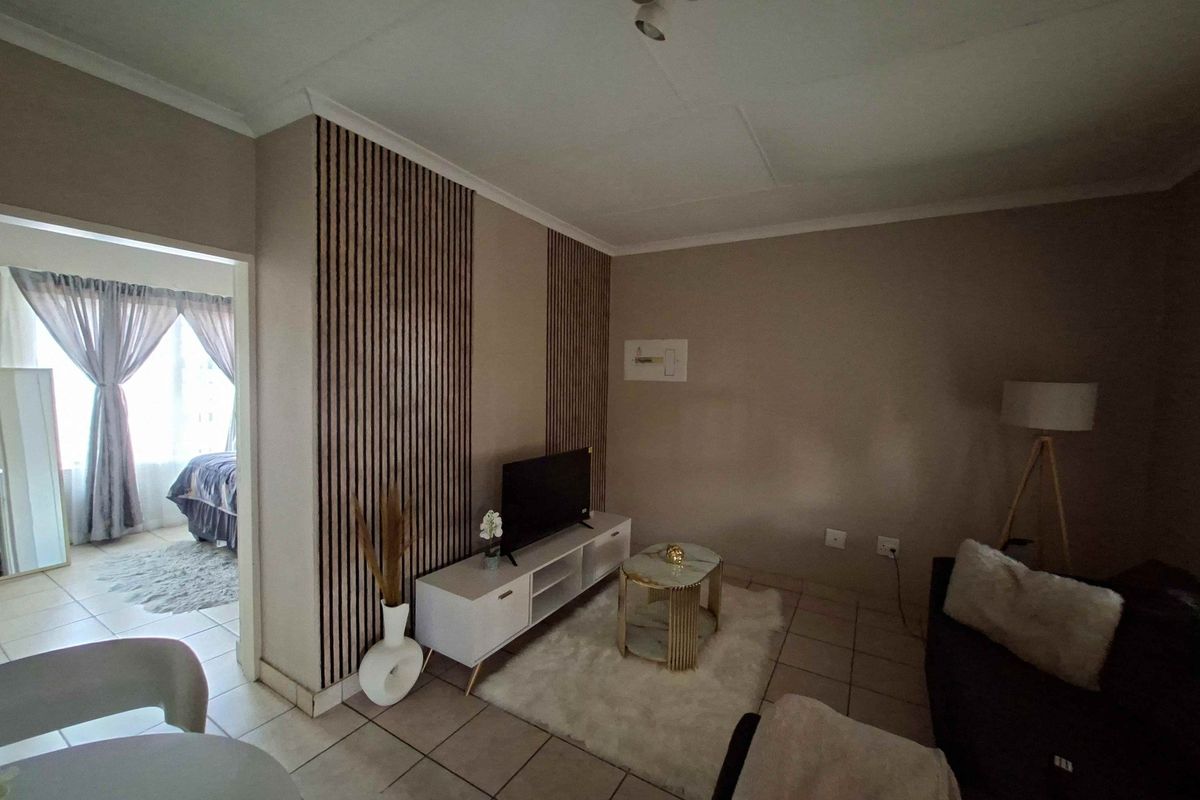 A cozy living room featuring decorative slatted wood wall paneling and neutral tiled flooring, with an open transition to the adjacent bedroom area.