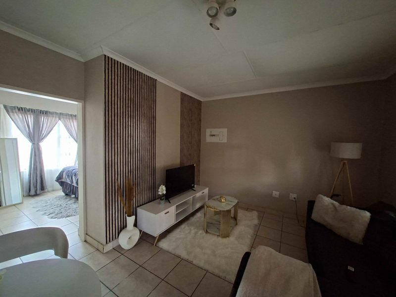 A cozy living room featuring decorative slatted wood wall paneling and neutral tiled flooring, with an open transition to the adjacent bedroom area.