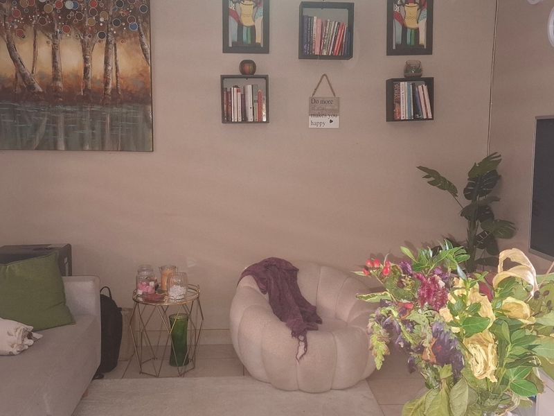 A cozy living room featuring neutral wall tones, roller blinds, and a wall-mounted television setup.