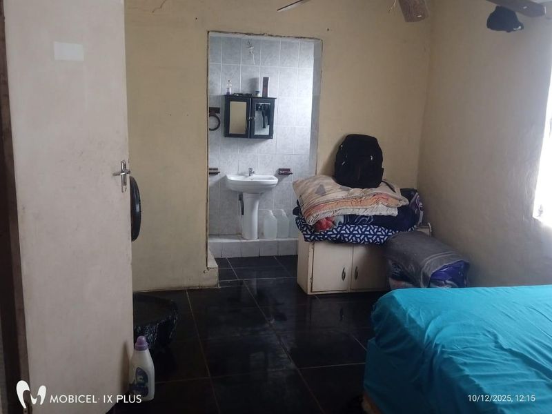 A bedroom featuring an en-suite bathroom area with a pedestal basin, tiled flooring, and ceiling fan, requiring cosmetic updates and wall repairs.