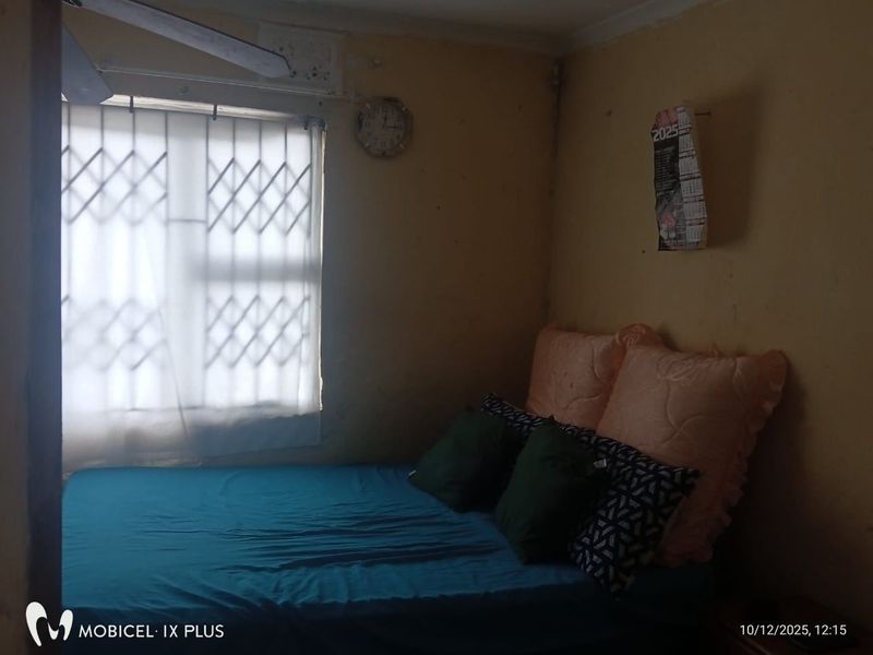 A bedroom featuring a security gate on the window and a ceiling fan, currently requiring cosmetic updates and wall repairs.