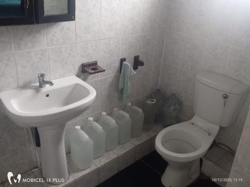 A functional bathroom featuring a pedestal washbasin and a standard toilet, finished with ceramic wall tiling.