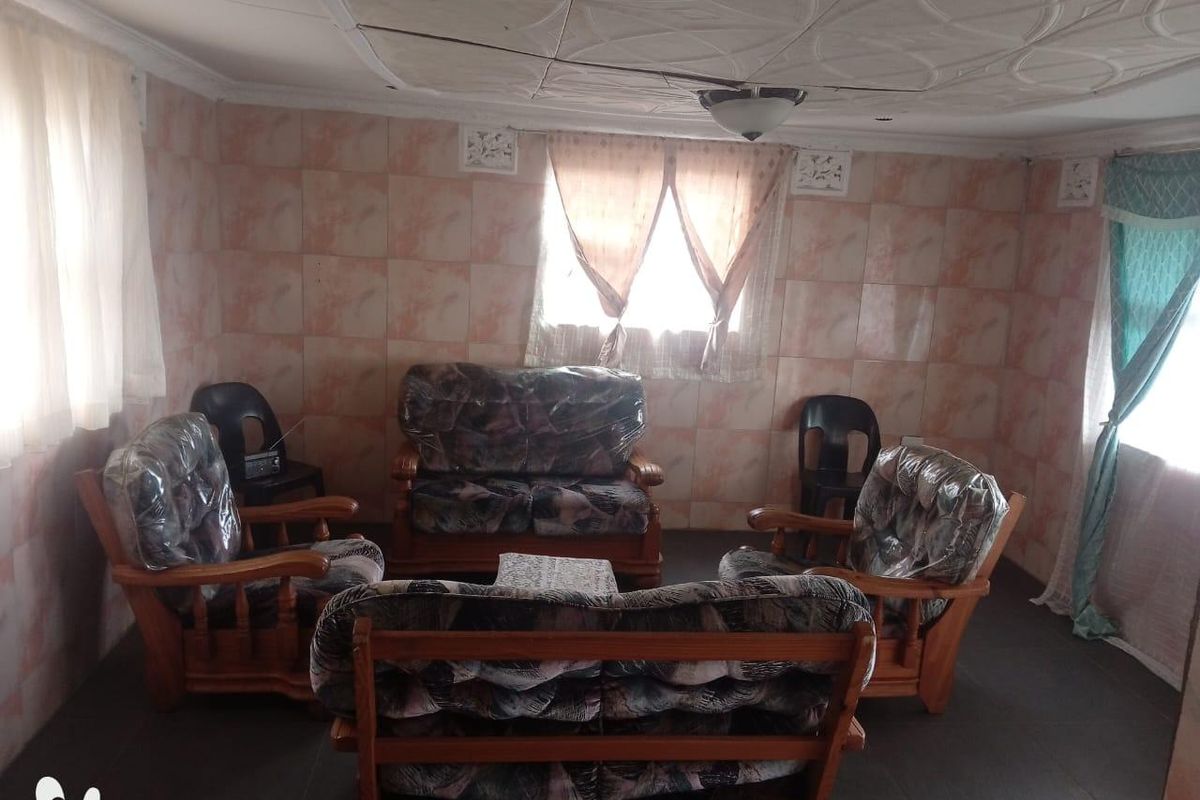 Living room featuring tiled walls, decorative ceiling tiles, and a ceiling fan. The space requires cosmetic updates to modernize the finishes.