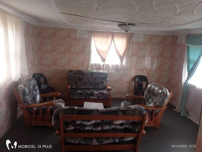 Living room featuring tiled walls, decorative ceiling tiles, and a ceiling fan. The space requires cosmetic updates to modernize the finishes.