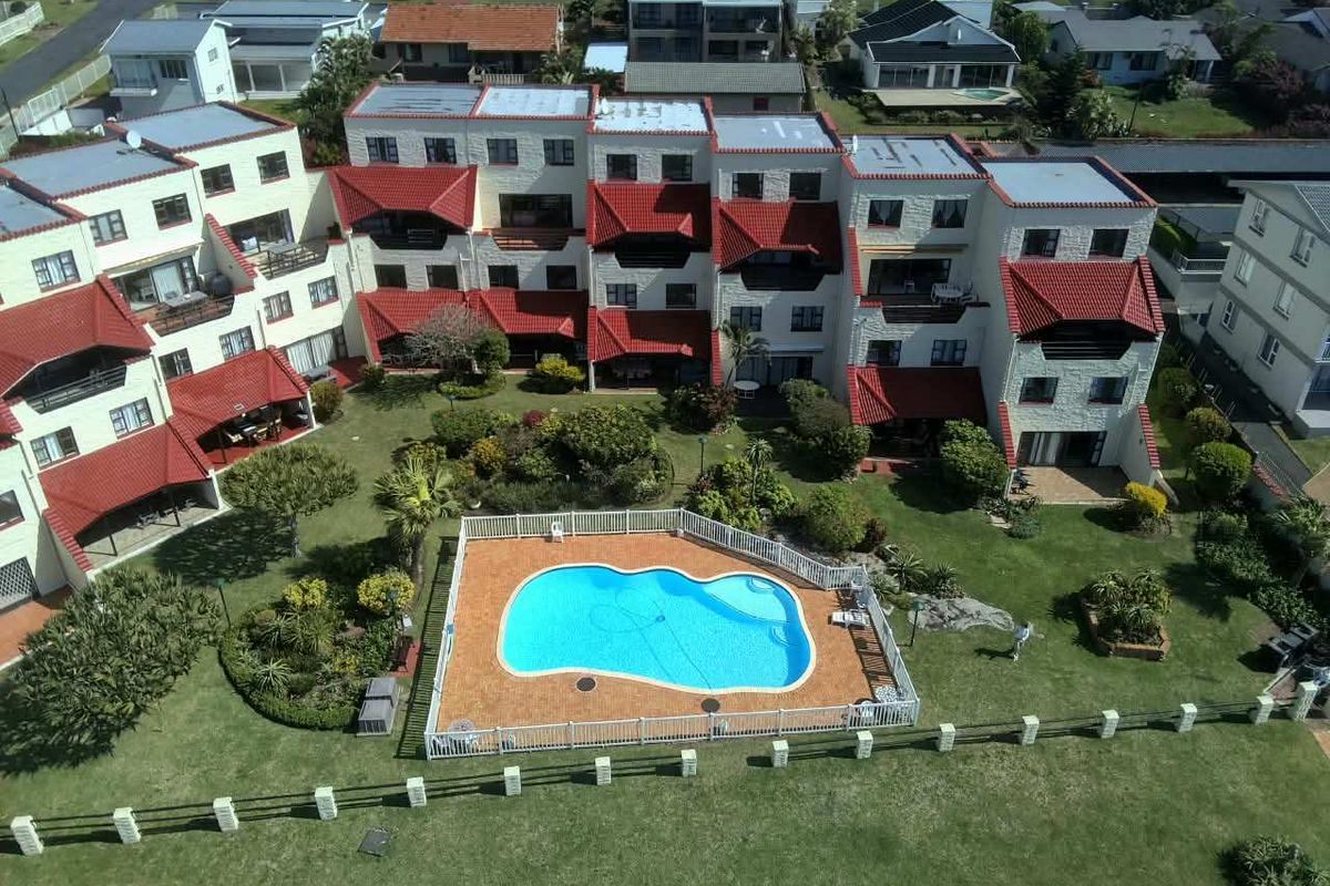 Aerial view of the apartment complex featuring a central swimming pool, landscaped gardens, and multi-level residential units with tiled roofs.