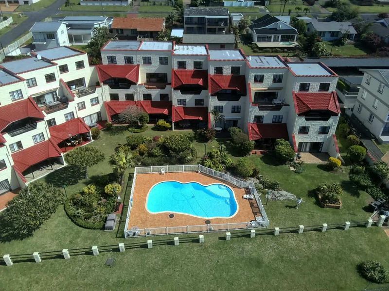 Aerial view of the apartment complex featuring a central swimming pool, landscaped gardens, and multi-level residential units with tiled roofs.
