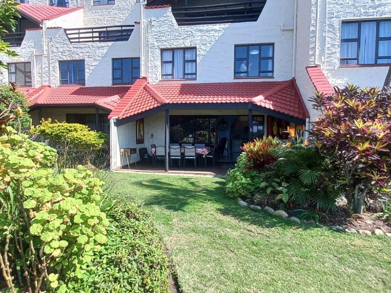 Rear view of the apartment complex featuring a covered patio area, tiled roofing, and a well-maintained private garden space.