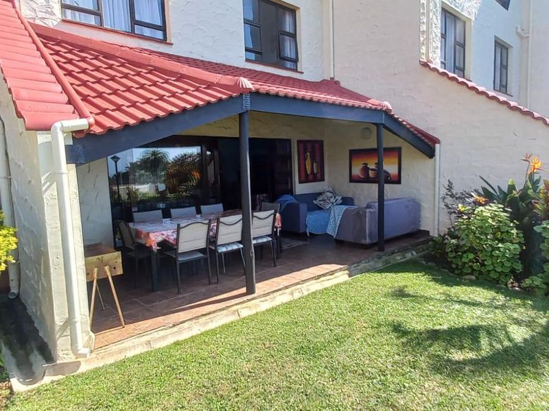 A covered patio area featuring tiled flooring and direct access to the apartment interior through sliding glass doors, overlooking a private garden space.
