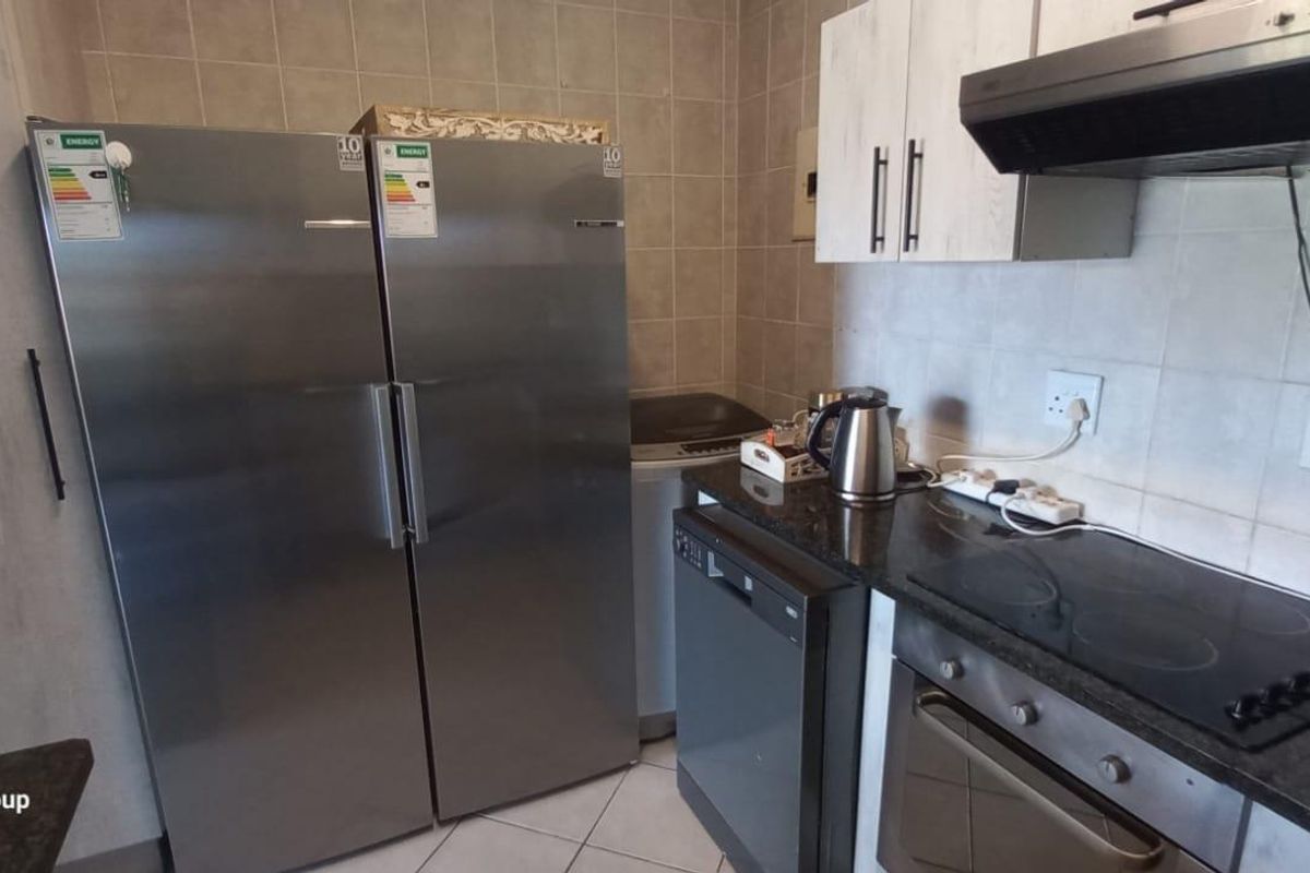 A functional kitchen featuring granite countertops, built-in cabinetry, an electric hob, oven, and extractor fan with tiled backsplash and flooring.