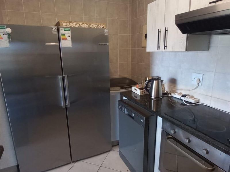 A functional kitchen featuring granite countertops, built-in cabinetry, an electric hob, oven, and extractor fan with tiled backsplash and flooring.