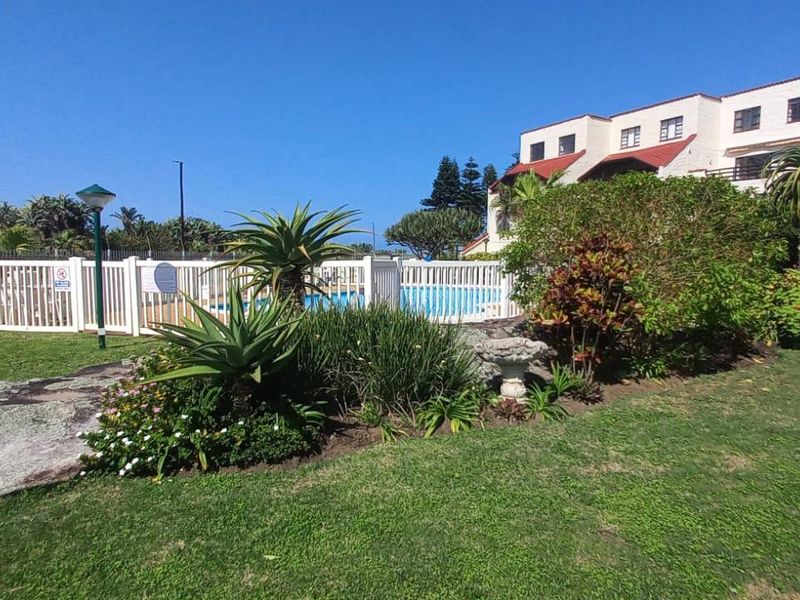 A well-maintained communal swimming pool area surrounded by landscaped gardens and lawn within the apartment complex grounds.