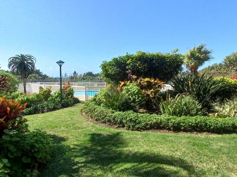 A well-maintained communal garden area featuring lush landscaping and a swimming pool in the background.
