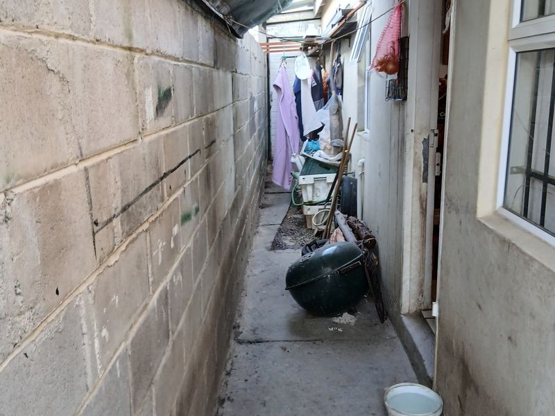 A narrow side passage featuring a concrete block boundary wall and concrete pathway, currently used as a utility and storage area.