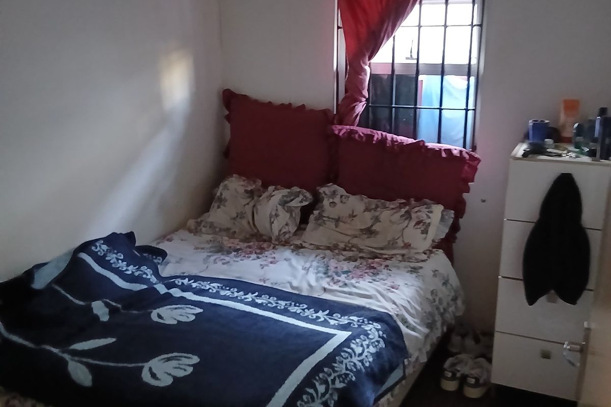 A compact bedroom featuring tiled flooring and a window fitted with security bars.