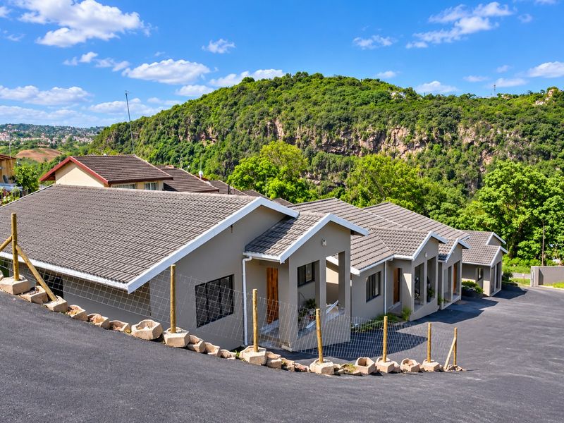 A row of modern residential units featuring tiled roofs and paved driveways, set against a scenic hillside backdrop.