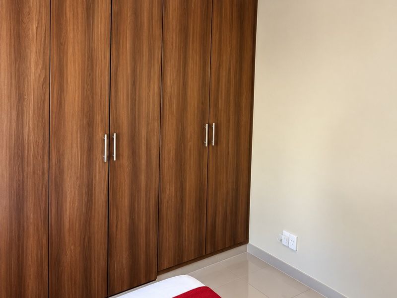 A clean bedroom featuring floor-to-ceiling wood-finish built-in wardrobes and neutral tiled flooring.