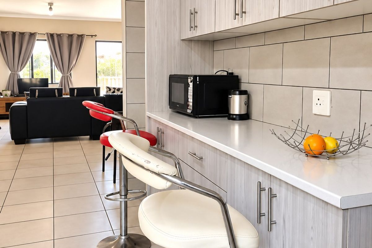 Modern open-plan kitchen area featuring light wood-grain cabinetry, sleek countertops, and neutral ceramic floor tiles, seamlessly flowing into the adjacent living space.