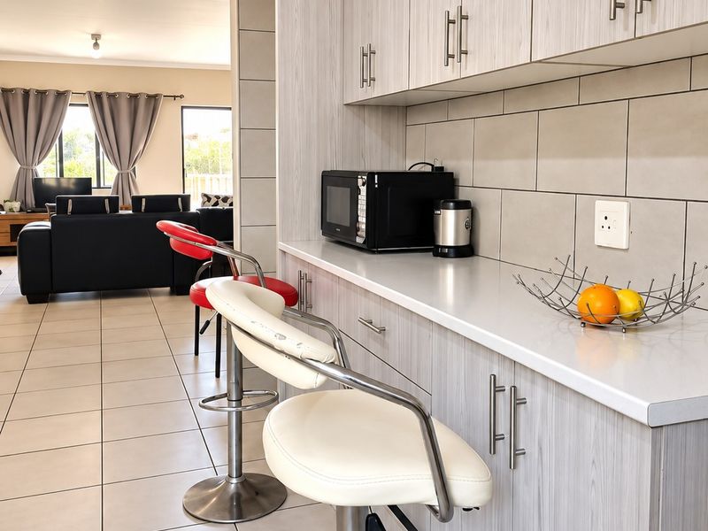 Modern open-plan kitchen area featuring light wood-grain cabinetry, sleek countertops, and neutral ceramic floor tiles, seamlessly flowing into the adjacent living space.