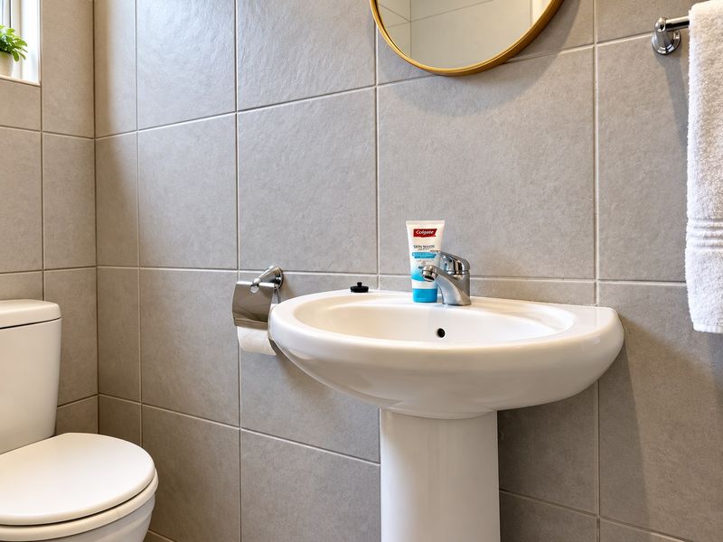 A modern bathroom featuring a pedestal basin with chrome mixer tap, toilet, and neutral ceramic wall tiling.