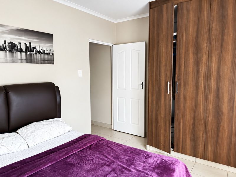 A well-maintained bedroom featuring neutral wall tones, tiled flooring, and a large built-in wooden wardrobe.