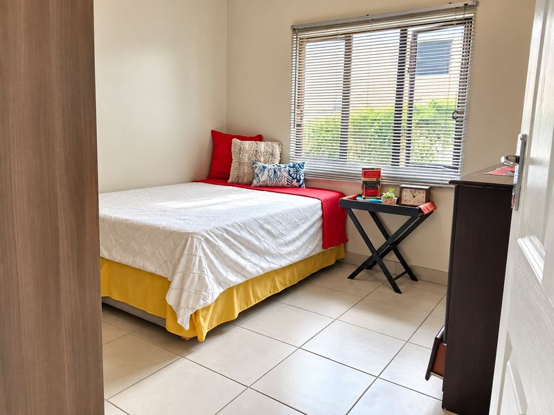 A well-maintained bedroom featuring neutral tiled flooring, a built-in cupboard, and a window fitted with venetian blinds for adjustable natural light.
