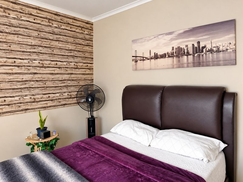 A cozy bedroom featuring a decorative wood-effect feature wall and neutral paint tones, providing a comfortable and well-maintained sleeping space.