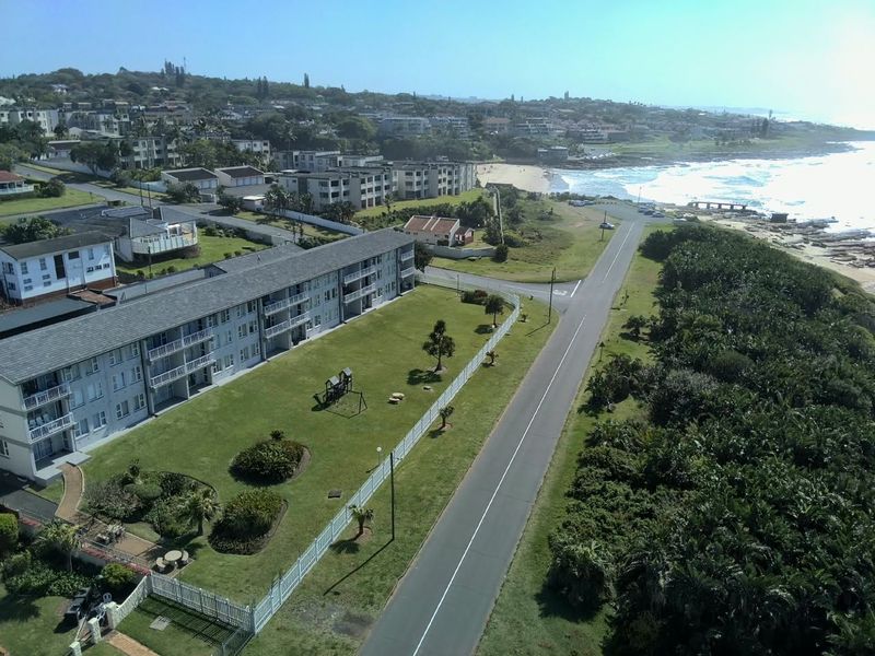 Aerial view of the apartment complex, featuring communal grounds, perimeter fencing, and proximity to the coastline and local beach.