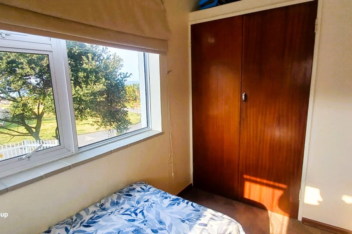 A bedroom featuring a built-in wooden wardrobe and a window with a roller blind, offering natural light and exterior views.