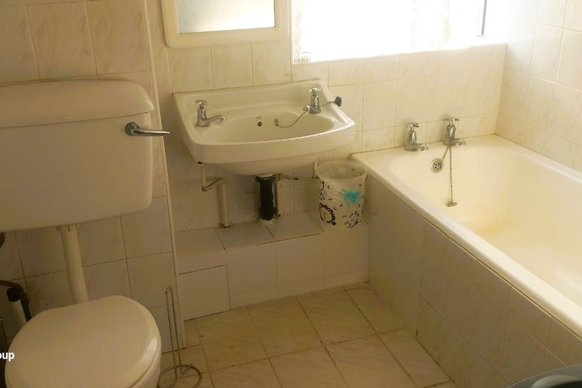 A dated bathroom featuring a standard bathtub, pedestal basin, and toilet with original wall and floor tiling.