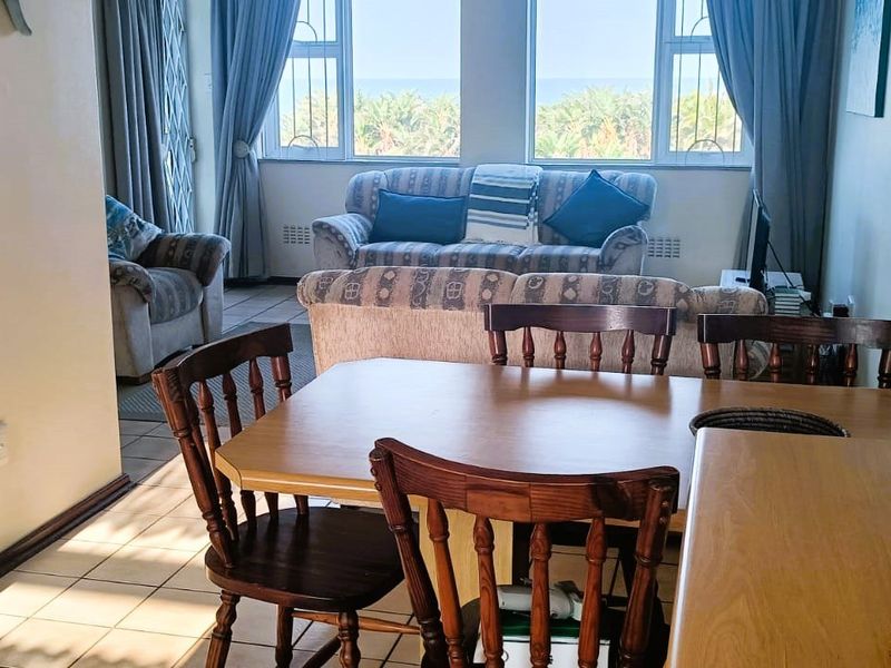 Open-plan living and dining area featuring tiled flooring, large windows with natural light, and an integrated kitchen space.
