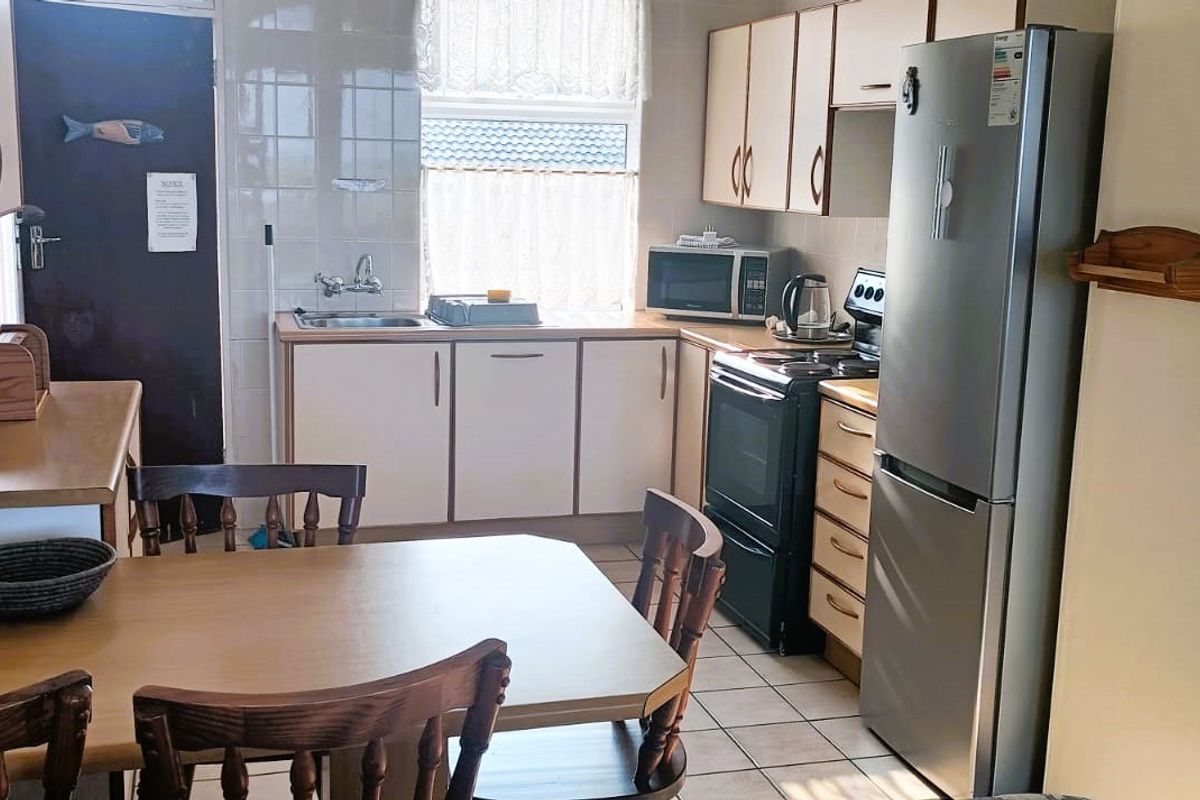 A functional kitchen featuring tiled flooring, built-in cabinetry, a tiled backsplash, and a stainless steel sink, offering a practical layout for daily use.