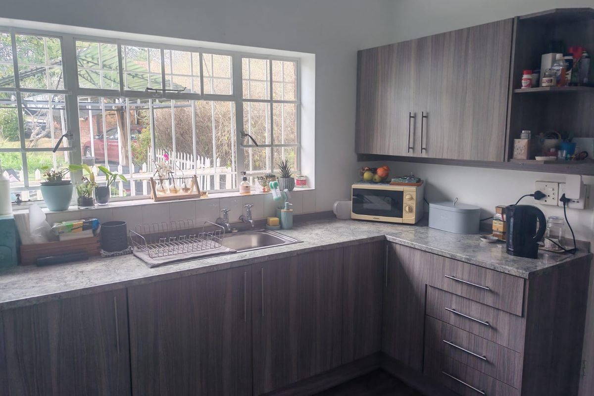 A functional kitchen featuring modern wood-grain laminate cabinetry, stone-look countertops, and a stainless steel sink positioned under a window with security bars.