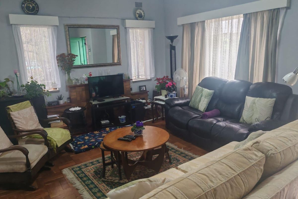 A comfortable living room featuring classic parquet flooring, built-in wooden cabinetry, and large windows with traditional pelmets, offering a warm and inviting atmosphere.
